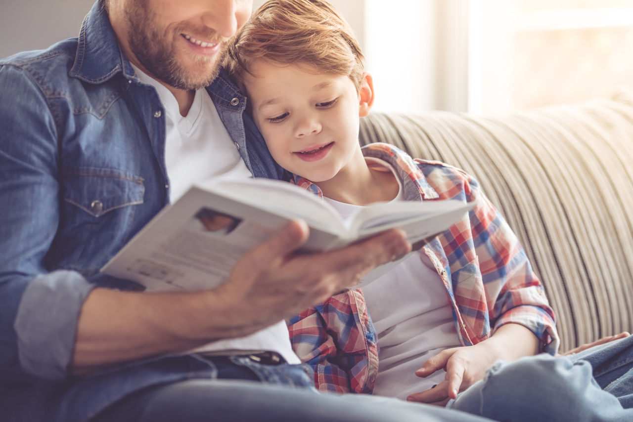 Father and son reading a book and smiling while spending time together at home