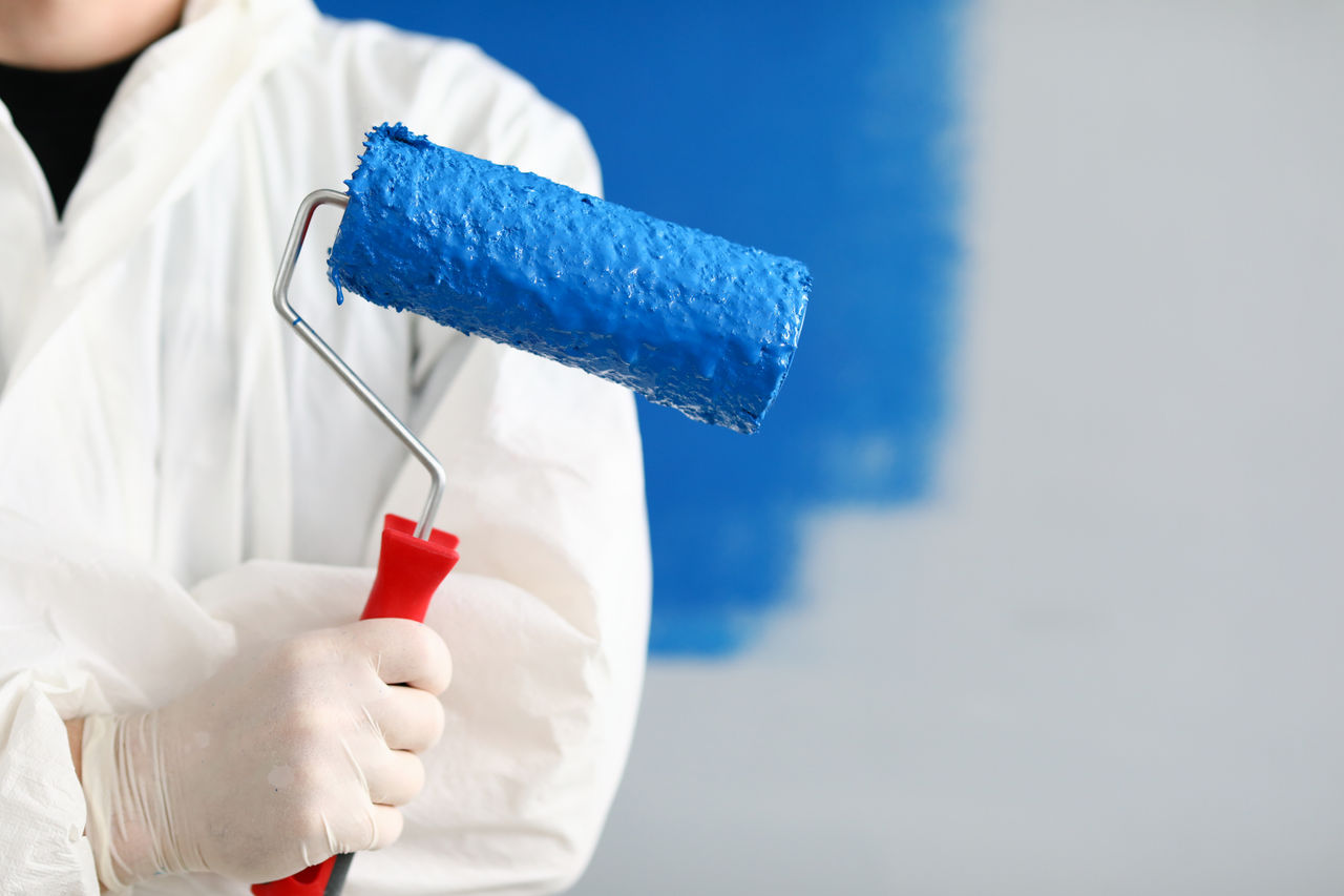 Close-up of person painter holding roller covered in blue paint. Professional worker wearing protective uniform and gloves. Copy space in right side. Renovation concept; Shutterstock ID 1743262391; purchase_order: CON; job: P&C - Decorative paints, main applications; client: ; other: 