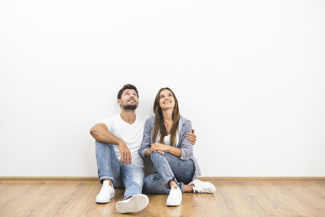 The happy couple sit near the white wall; Shutterstock ID 717572647