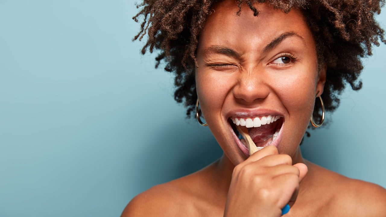 Close up shot of happy joyful funny dark skinned young woman has Afro hair brushes teeth actively with toothbrush, opens mouth broadly, blinks eye, shows bare shoulders, cares of oral hygiene; Shutterstock ID 1335284804; purchase_order: COG PC Oral Care Brochure; job: Oral Care Brochure; client: Omya; other: Phana Tuon
1335284804